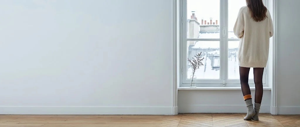 Femme de dos à la fenêtre d'un appartement parisien enneigé, en collant Frileuse